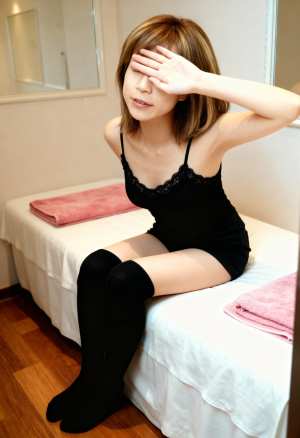 黒いレースのキャミソールと黒のサイハイソックスを履いて、右手で目を覆いベッドに座る若...。