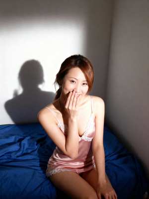 薄暗い部屋のベッドに座り、白いレースのトリムが付いたピンクのサテンのキャミソールを着...。