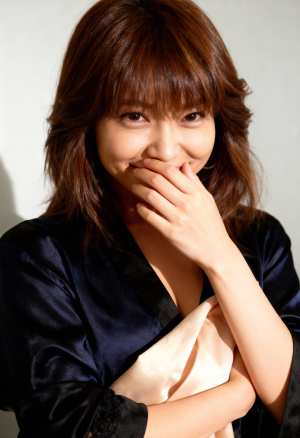 ダークブルーのサテンのローブを着て、手で口を覆い、遊び心のある表情をしたアジア系の若...。