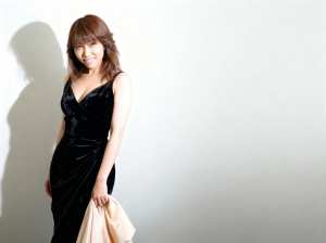 黒のベルベットのフォーマルなドレスを着て、真っ白な壁に立ち、左手にベージュの布を持っ...。