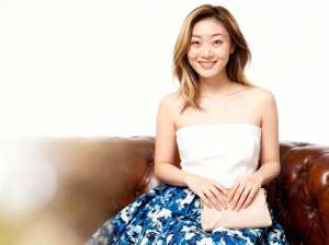 白いストラップレスのトップスと青い花柄のスカートを着て、リラックスしたポーズで茶色の...。