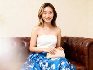 白いストラップレスのトップと青い花柄のスカートを着て、リラックスしたポーズで茶色の革...。