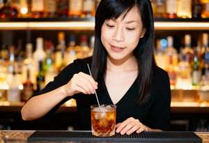 長い黒髪のアジア系の若い女性がバーカウンターに座り、ストローを手にアイスティーの入っ...。