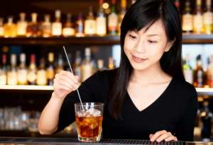 黒いVネックのシャツを着た長い黒髪の若いアジア人女性が、薄暗いバーのバーカウンターに...。