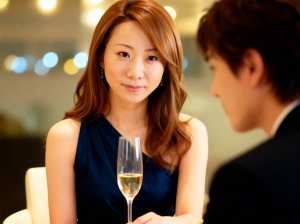 ネイビーブルーのノースリーブのドレスを着て、白ワインのグラスを前にテーブルに座ってい...。