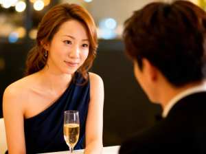 ネイビーブルーのワンショルダードレスを着てシャンパンを飲みながらテーブルに座り、正装...。