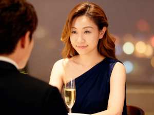 ネイビーブルーのワンショルダードレスを着た若い女性がシャンパングラスを前にテーブルに...。