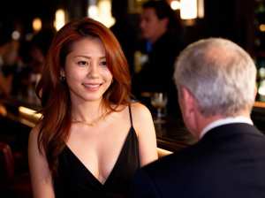 薄暗いレストランのバーに座っている男性に微笑む黒いドレスを着た女性を、正面から写実的...。