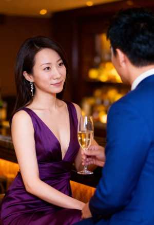 紫のドレスを着た女性がテーブルに座り、青いスーツを着た男性の前で白ワインを飲みながら...。