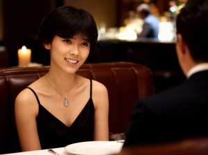 薄暗いレストランのテーブルに座り、カメラに向かって微笑みながら前に座っている男性と会...。