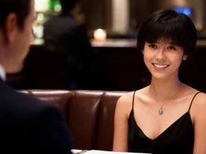 レストランのテーブルに座り、フォーマルな雰囲気の中で男性に微笑みかけている若い女性を...。