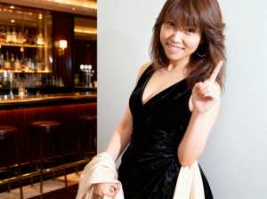 黒いベルベットのドレスを着た若い女性が画像の中央に立ち、自信に満ちた笑顔で親指を立て...。