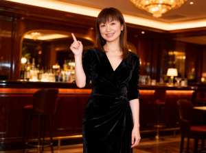 薄暗いバーに立ち、自信に満ちた笑みを浮かべて上を向いている若い女性のポートレート。