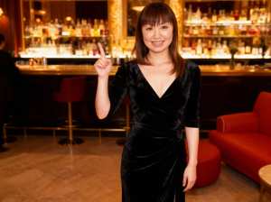 薄暗いバーの真ん中に立ち、親指を立てるジェスチャーをする若い女性のポートレート。