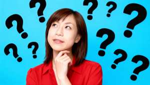 明るい青色の背景に疑問符で囲まれた、思慮深い表情を持つ若いアジア人女性のポートレート。