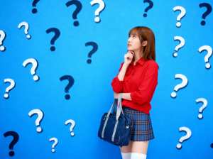 青い背景の前に疑問符の付いた若い女性が立っており、赤いボタンアップ シャツ、格子縞の...。