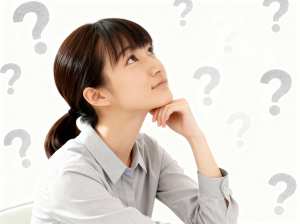 画像の中央には、ライトグレーの襟付きシャツを着た、思慮深い表情をした若い女性が座っています。