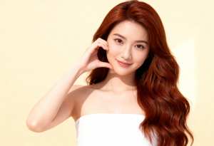 シンプルな明るい黄色の背景に対して、画像の中央に立つ、長くウェーブのかかった赤茶色の...。