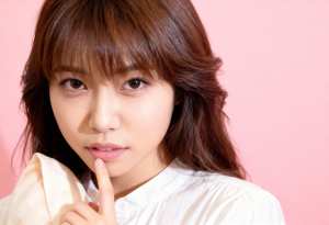 柔らかいピンクの背景に、唇に指を当ててポーズをとる、思慮深い表情を持つ若い女性のクロ...。