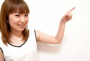 右手の人差し指を上に向け、明るい表情をしたアジア系の若い女性。