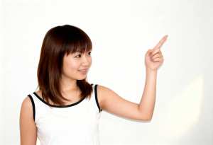 肩までの長さのストレートなボブヘアを持ち、人差し指を上に向けてわずかな笑みを浮かべた...。