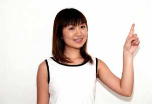 無地の白い背景の前に立つ、陽気な表情の若いアジア人女性。