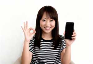 画像の中央に座っている若いアジア人女性は、右手に黒いスマートフォンを持ち、左手で「O...。