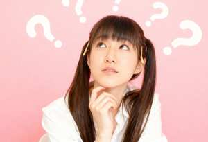 ピンクの背景に疑問符で囲まれた、長い茶色の髪と思慮深い表情をした若いアジア人女性を横...。