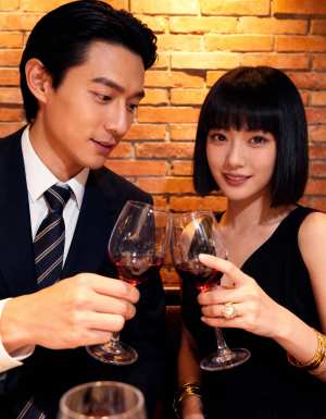 レンガの壁を背景にした薄暗いレストランで、ワイングラスで乾杯するカップルを正面から写...。