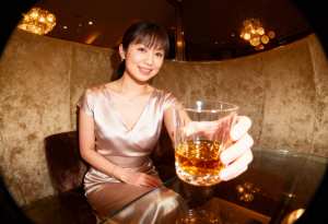 薄暗いレストランのガラスのテーブルに座り、ウィスキーのグラスを持った女性。