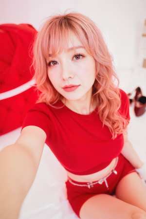 ピンクの髪の若い女性がミニマルな寝室の環境で自撮りをしている様子を、自撮りアングルか...。