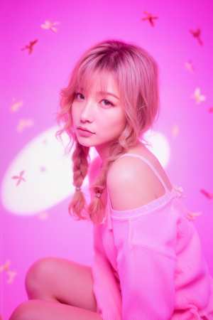 小さな蝶で飾られたピンクの背景に座っている、ブロンドの髪を三つ編みにした若い女性を横...。