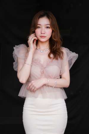 フリル袖のシアーピンクのトップスと白いペンシルスカートを着て、黒い背景に自信を持って...。