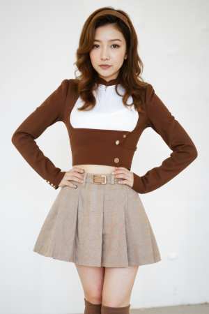 無地の白い壁の前で腰に手を当てて自信満々にポーズをとるアジア系の若い女性。