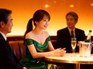 薄暗いレストランで、緑のスパンコールのドレスを着た女性がテーブルに座り、正装をした男...。