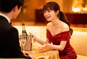 赤いスパンコールのドレスを着た若い女性が高級レストランのテーブルに座り、黒いスーツを...。