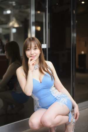 ガラスのドアの前で青いドレスを着てポーズをとり、カメラに向かって微笑む若い女性を、正...。