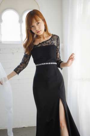 白い壁とアーチ型の窓のある明るい部屋に立つ黒いフォーマルなドレスを着た若い女性を、正...。