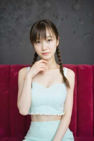 ライトブルーのクロップトップとミントグリーンのスカートを着て、赤いベルベットのソファ...。