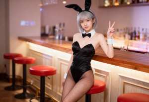 ウサギの格好をしてバーに座り、右手でピースサインをしている若い女性を横から撮った写実...。