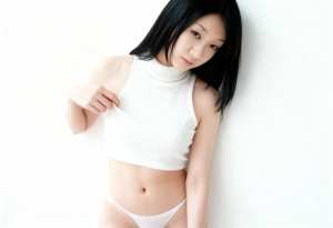 白いリブ編みのノースリーブトップスとそれに合ったパンティーを着て、無地の白い壁に向か...。