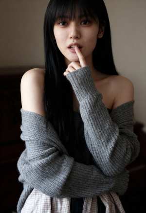 グレーのオフショルダー セーターとチェックのスカートを着て、唇の近くに指を当ててポー...。