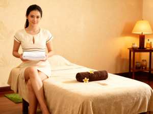 スパのマッサージ テーブルに座り、白いタオルの束を持っている女性。