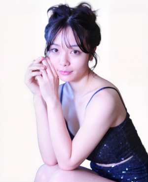 ネイビーブルーのスパンコールのトップを着て、瞑想的なポーズで床に座る若いアジア人女性...。