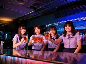 バーの後ろに立ち、ビールのグラスを手にカメラに向かって微笑む 4 人の若い女性を正面...。