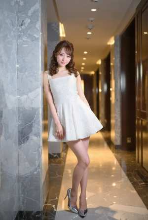 モダンな廊下の大理石の壁に立っている白いドレスを着た若い女性を横から撮影した写実的な写真。