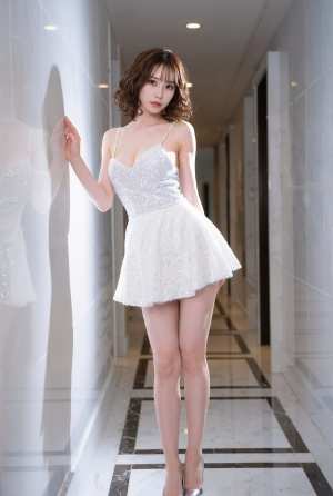 モダンな廊下のガラスの壁に立っている短い白いドレスを着た若い女性を横から撮った写実的な写真。