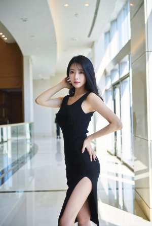 サイドにスリットの入ったタイトな黒のドレスを着て、モダンな建物で自信を持ってポーズを...。