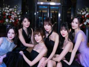 花で飾られた豪華なロビーの前で写真を撮る 7 人の若い女性のグループ。