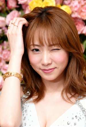 ピンクと黄色の花を背景にポーズをとる、ウェーブのかかった茶色の長い髪と温かい笑顔を持...。